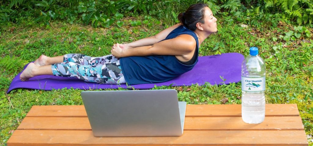 A Japanese women in sports wear doing online stretching and Yoga workout from home in the garden via a laptop computer.